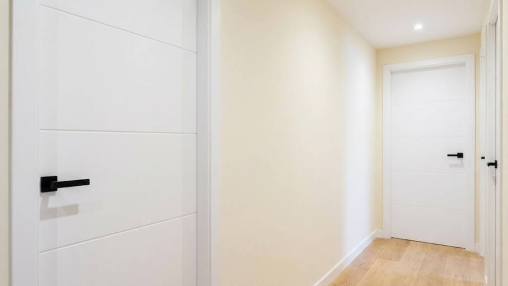 El «efecto túnel» tiene cura. En este piso del barrio de Gràcia, las antiguas puertas de sapelly oscurecían toda la vivienda. Nuestro equipo realizó una sustitución integral por puertas macizas lacadas en blanco mate con herrajes negros, logrando una modernización instantánea. Descubre cómo conseguimos ganar luz y aislamiento acústico en solo dos días y sin dañar las paredes.