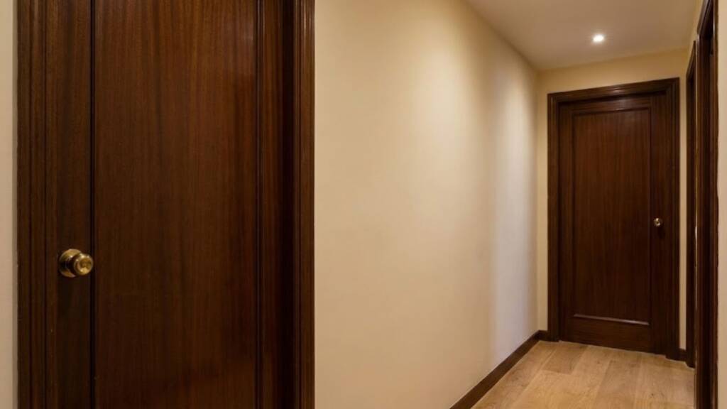 El «efecto túnel» tiene cura. En este piso del barrio de Gràcia, las antiguas puertas de sapelly oscurecían toda la vivienda. Nuestro equipo realizó una sustitución integral por puertas macizas lacadas en blanco mate con herrajes negros, logrando una modernización instantánea. Descubre cómo conseguimos ganar luz y aislamiento acústico en solo dos días y sin dañar las paredes.