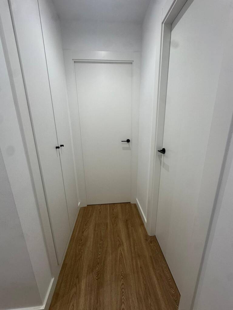 Renovación integral de carpintería y pavimentos en vivienda de El Masnou. Instalación de parquet laminado tono roble, puertas lacadas blancas y armarios a medida con herrajes de diseño en negro mate.