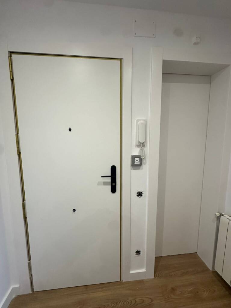 Renovación integral de carpintería y pavimentos en vivienda de El Masnou. Instalación de parquet laminado tono roble, puertas lacadas blancas y armarios a medida con herrajes de diseño en negro mate.