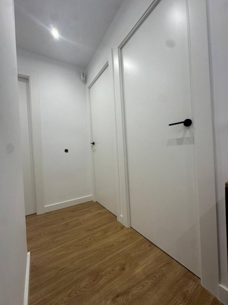 Renovación integral de carpintería y pavimentos en vivienda de El Masnou. Instalación de parquet laminado tono roble, puertas lacadas blancas y armarios a medida con herrajes de diseño en negro mate.