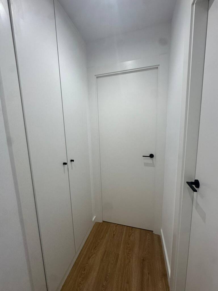 Renovación integral de carpintería y pavimentos en vivienda de El Masnou. Instalación de parquet laminado tono roble, puertas lacadas blancas y armarios a medida con herrajes de diseño en negro mate.