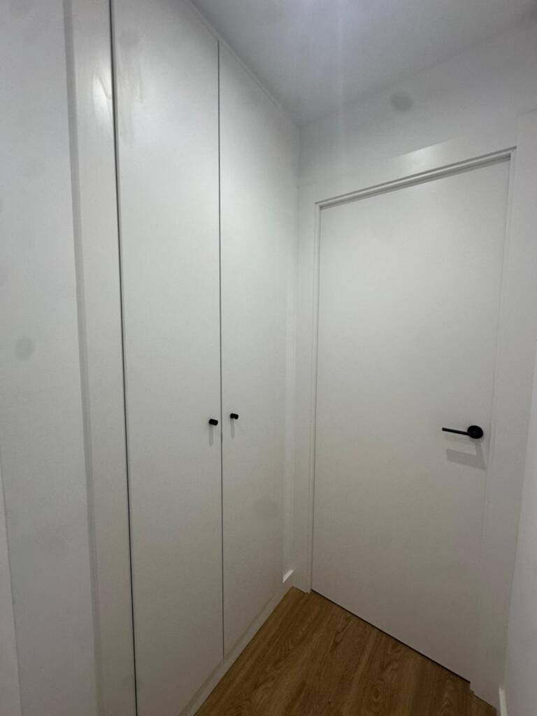 Renovación integral de carpintería y pavimentos en vivienda de El Masnou. Instalación de parquet laminado tono roble, puertas lacadas blancas y armarios a medida con herrajes de diseño en negro mate.